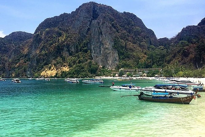Boats moored off the white-sand beach of Phi Phi Don beneath a green limestone cliff