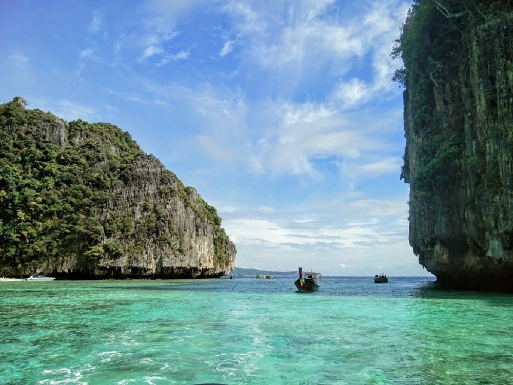 A longtail boat in clear turquoise water between two Phi Phi limestone cliffs