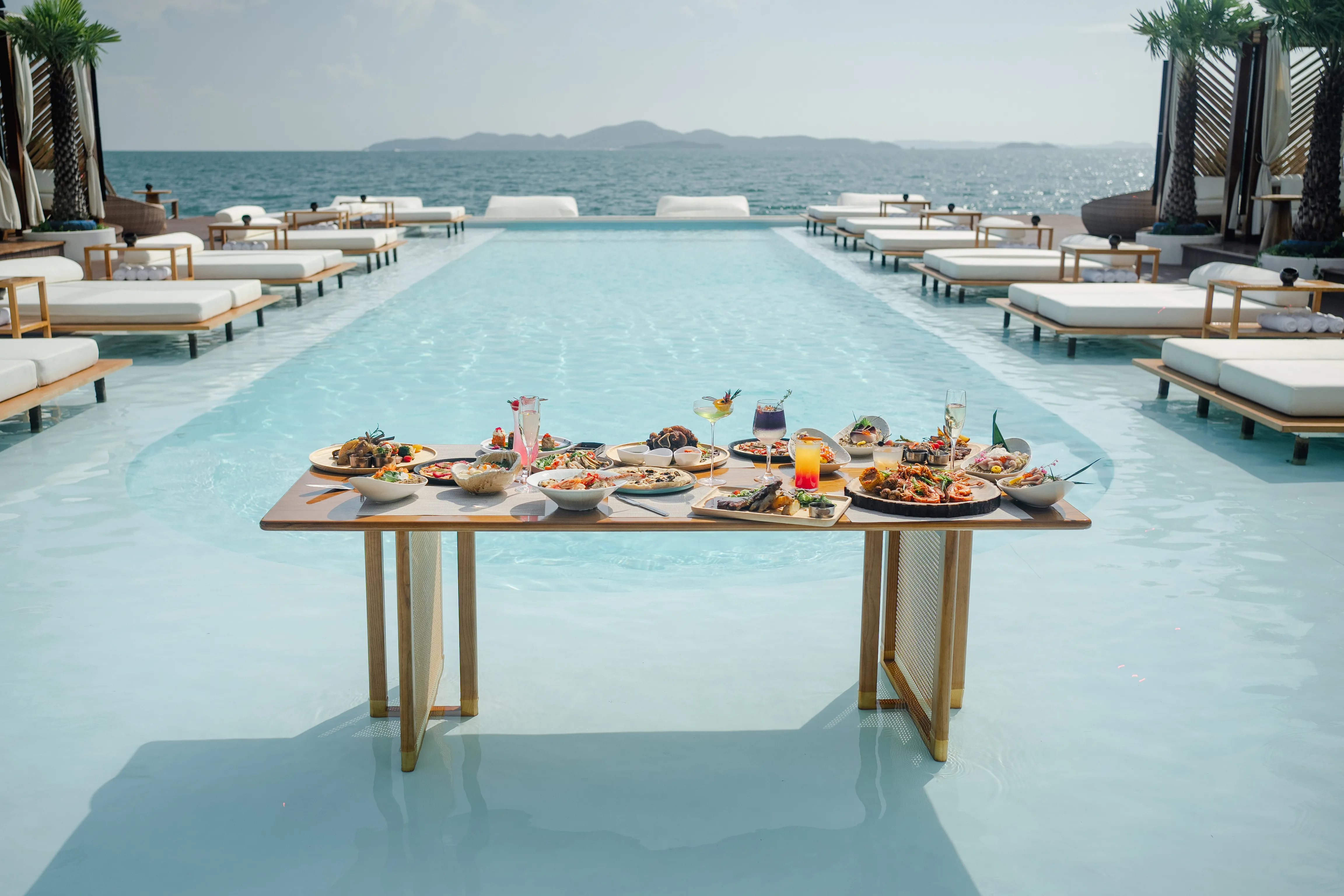 Infinity pool and sun beds overlooking the sea at Sina Beach Club, the floating beach club in Pattaya