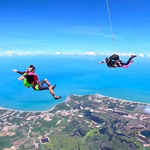 Tandem and solo skydivers in freefall over the ocean near Pattaya